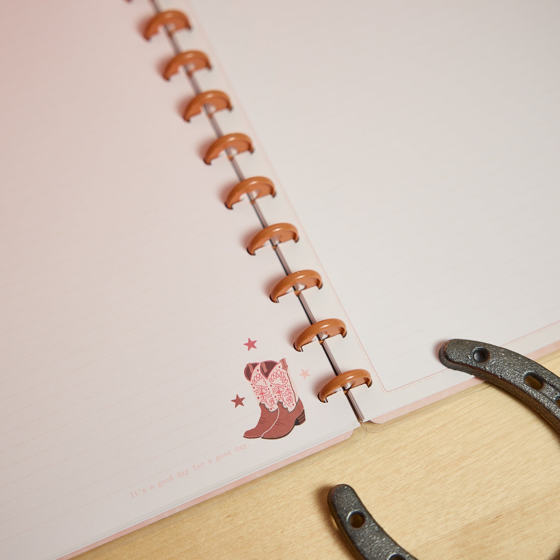 Close-up of an open Western Bloom - Dotted Lined Big Notebook - 60 Sheets showing the disc-bound design, subtle dotted lined pages, and a decorative illustration of cowboy boots with stars on the bottom corner.