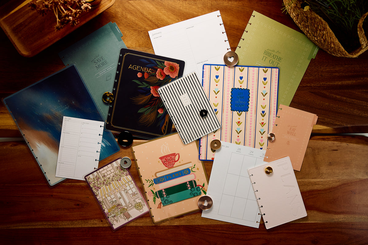 Flat lay of colorful disc bound planners notebooks filler paper journal pages and decorative stickers arranged on a wooden table beside loose planner discs