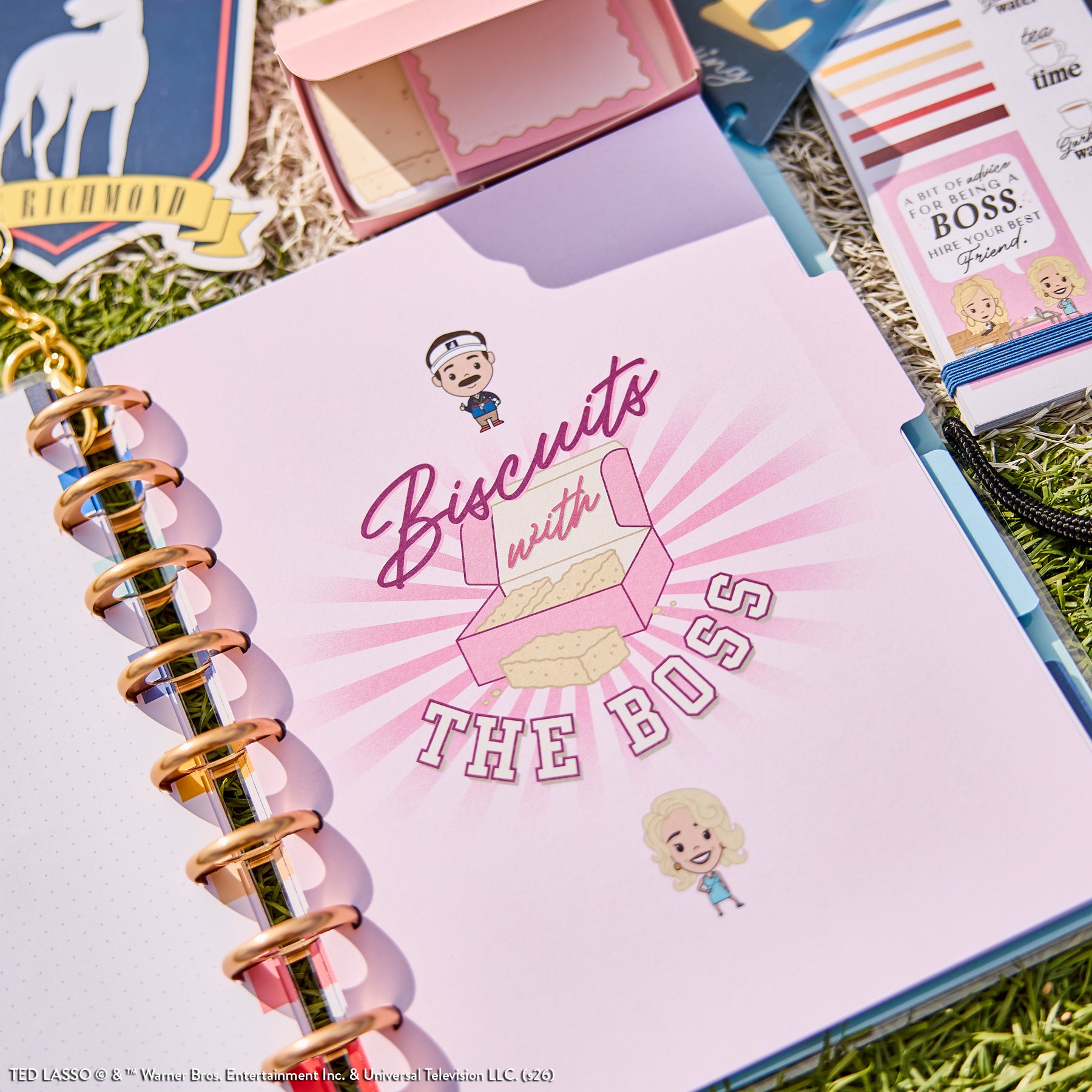 Open pink disc bound planner page featuring "Biscuits with The Boss" design with small cartoon characters and surrounded by stickers and notes from the Ted Lasso - Be Happy Box collection.