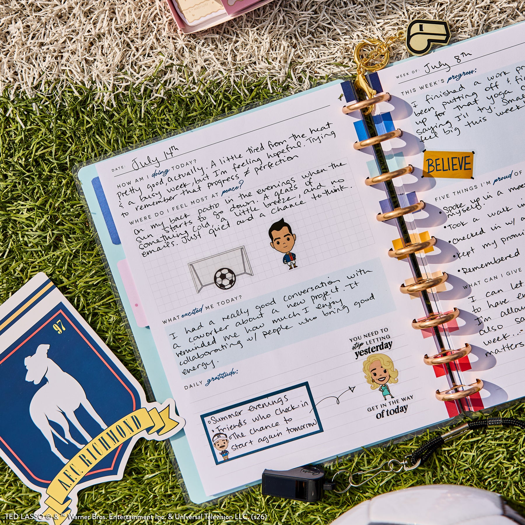 Open Ted Lasso - Be Happy Box journal featuring a disc-bound planner with guided journal entries, stickers, and colorful dividers on grass, alongside a Richmond-themed card.
