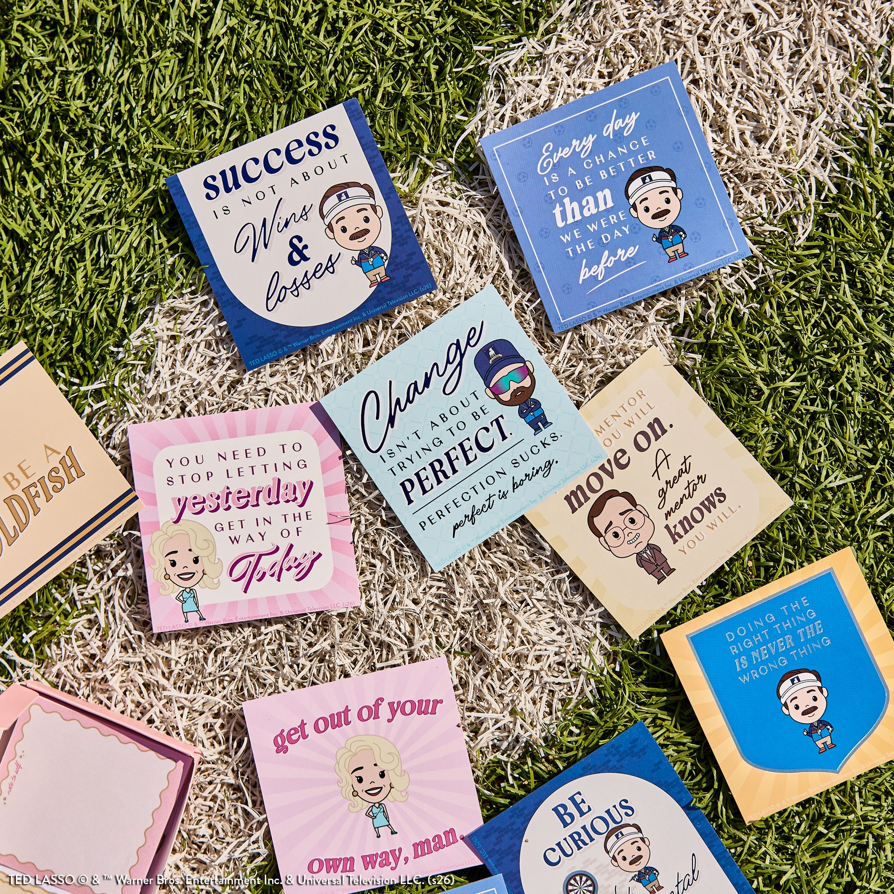 Ted Lasso - Be Happy Box featuring colorful sticky notes with motivational quotes and cartoon characters from Ted Lasso displayed on grass and turf background.